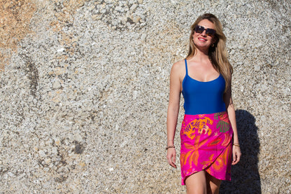 Woman wearing a blue costume and colorful pink sarong skirt standing against a textured stone rock.